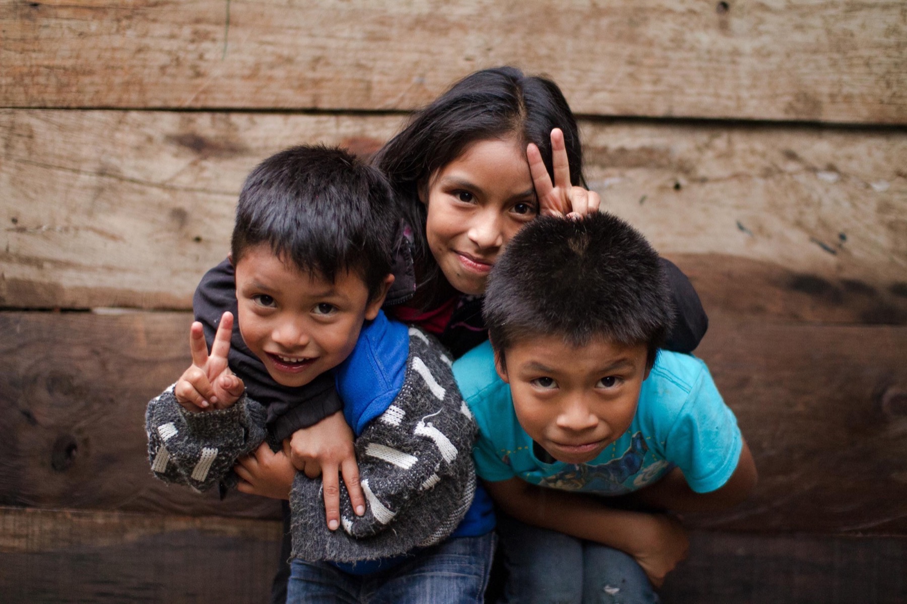 Three children smiling in front of a wooden wall