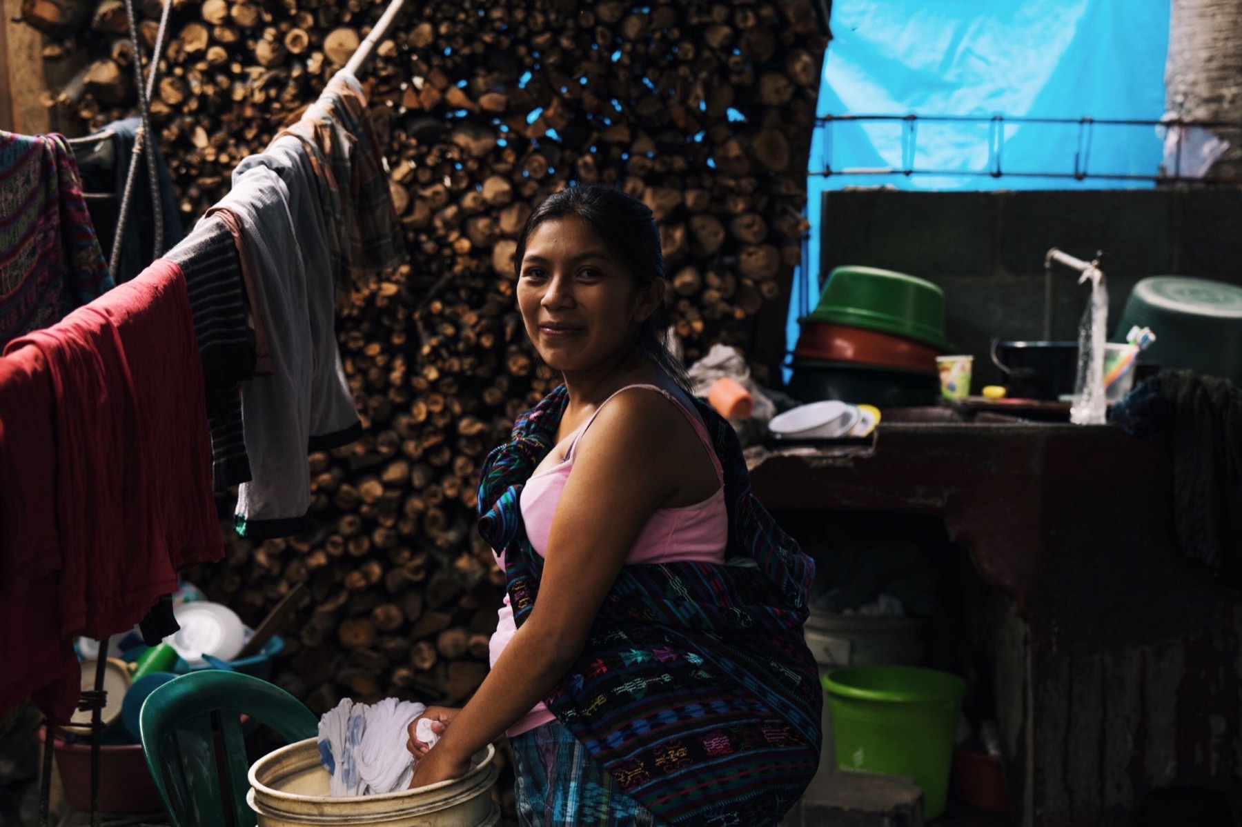 A young woman washing clothes beside a stack of firewood