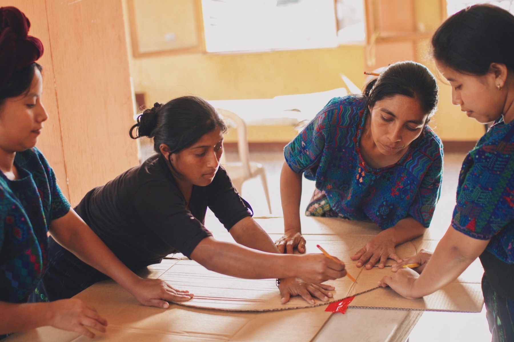 Four women drawing a pattern together on a sheet of cardboard